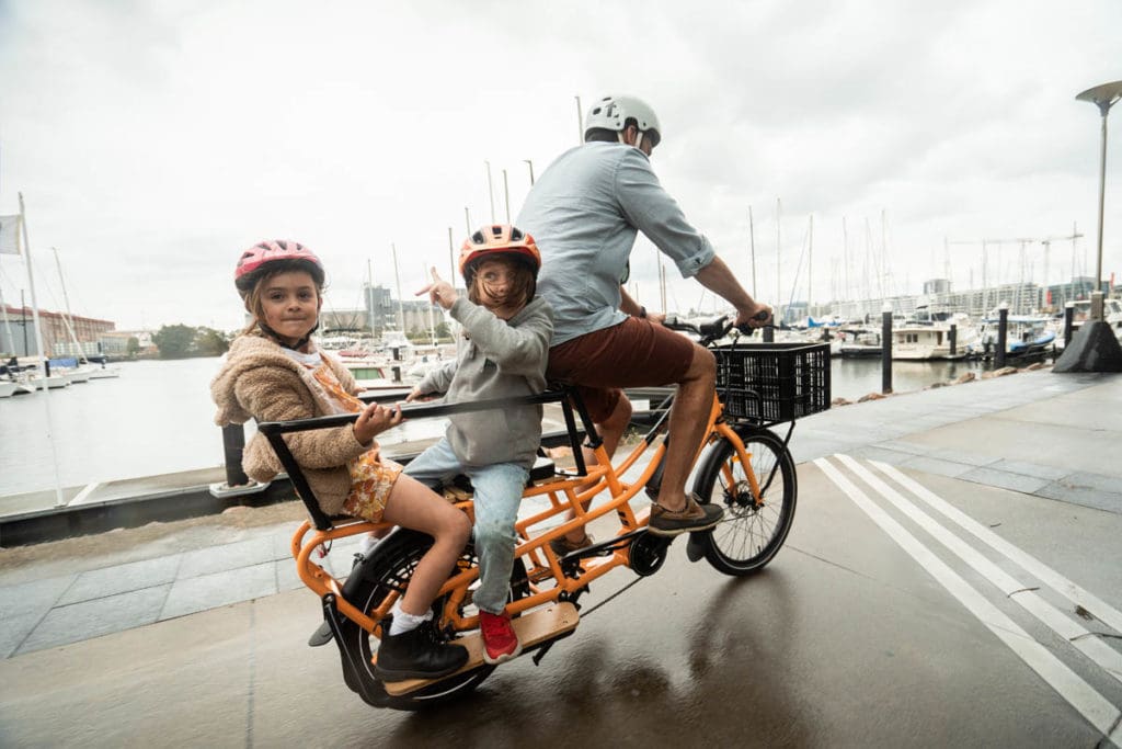 Aldult riding Evamos Cargo Bike with two kids on the back.