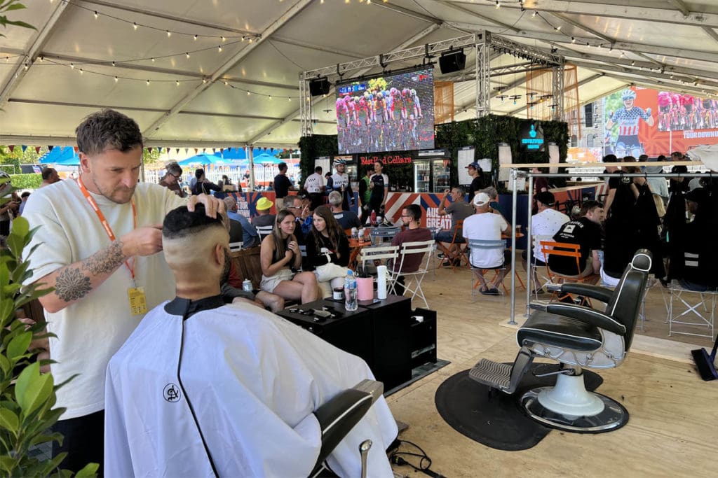 A barber shaving man's head in outdoor setting