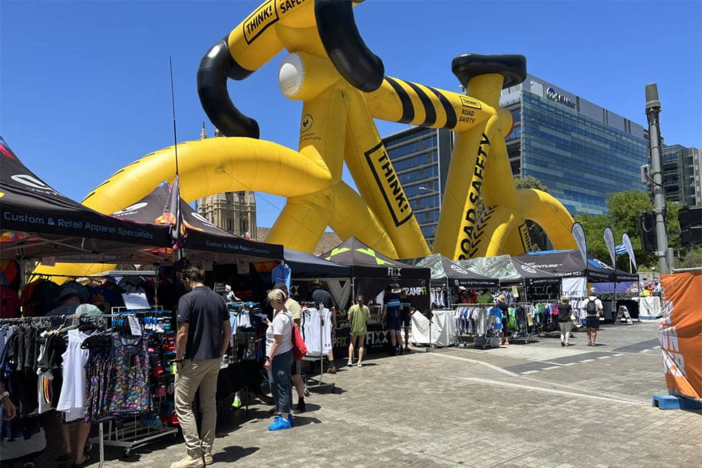 Outdoor exhibit stalls with large bicycle inflatable in background.