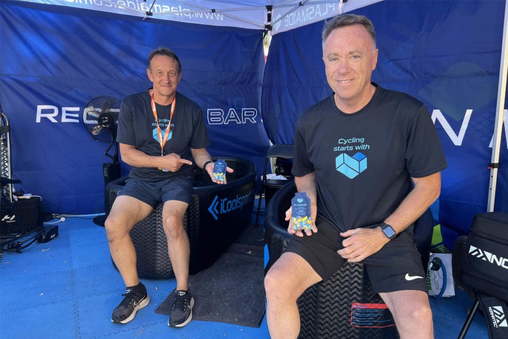 Two men sitting on ice baths holding sports supplement packet.