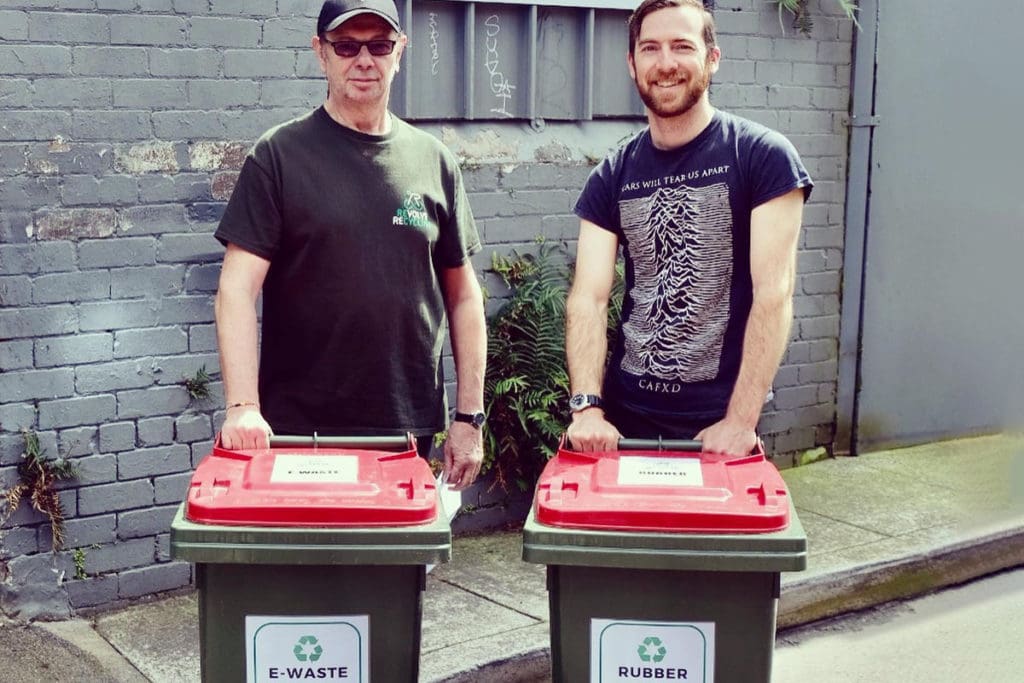 Two men on street with e-waste and rubber recycle bins