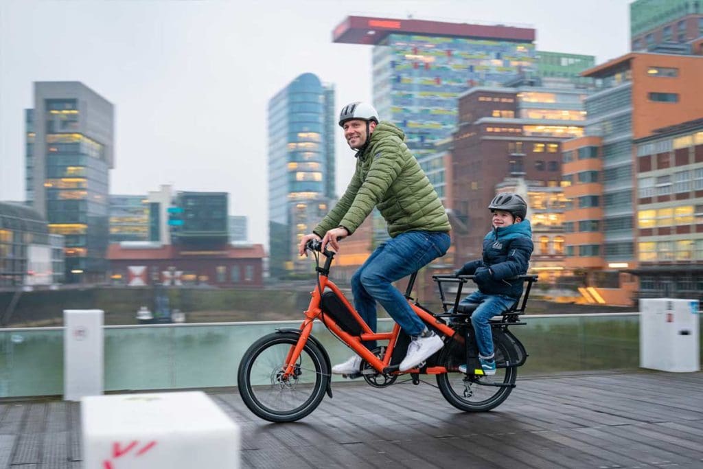 Man and child riding e-cargo bike in city