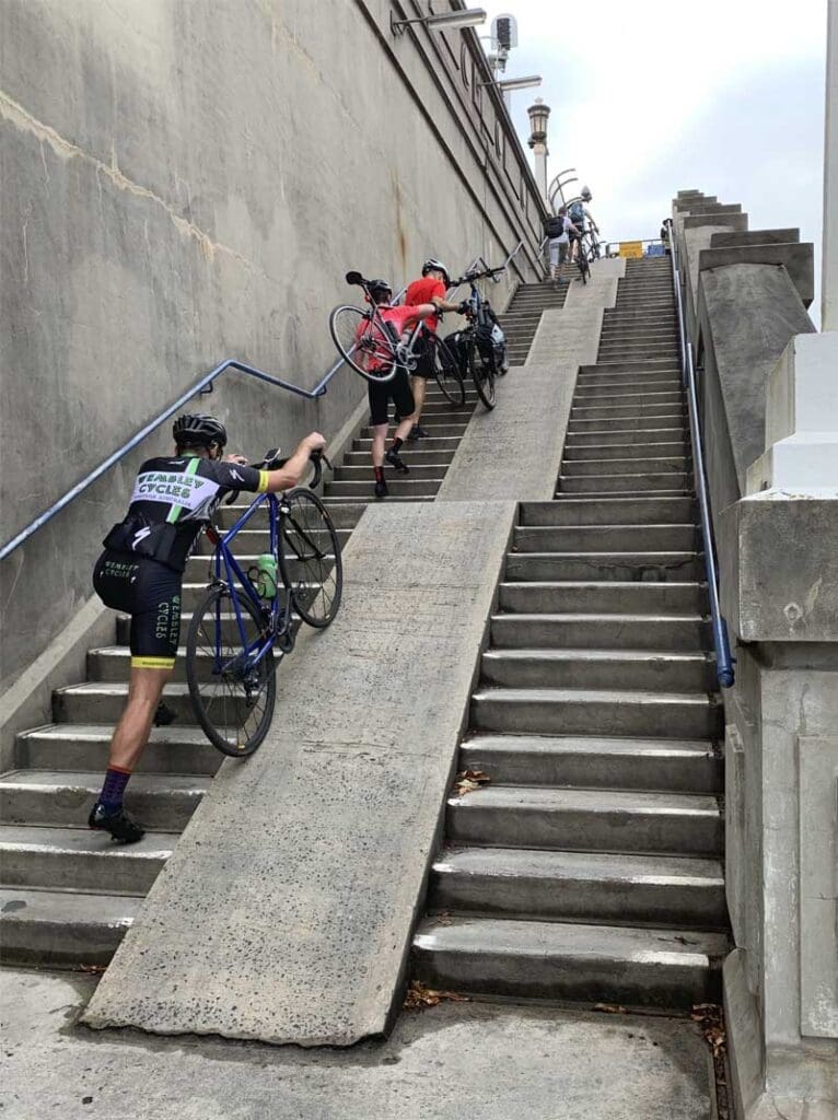 Cyclists pushing bikes up a stair case