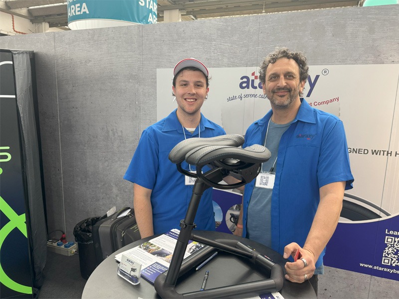 Two men standing with bicycle seat on display at bike expo