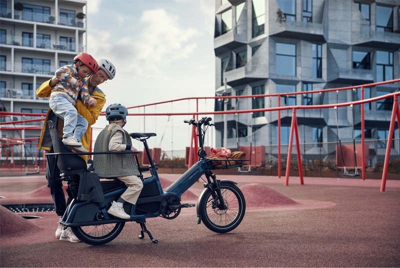 Person in playground setting loading two children into cargo bike.