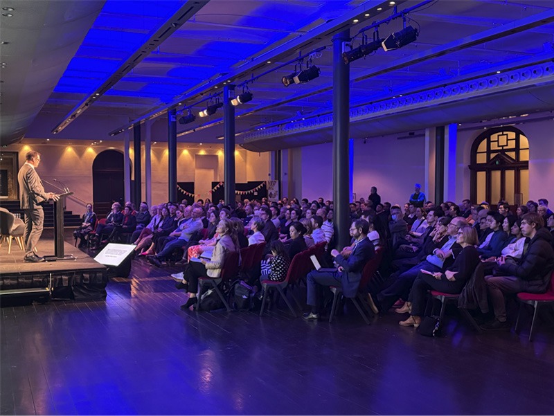 Side view of a person speaking on stage to an audience