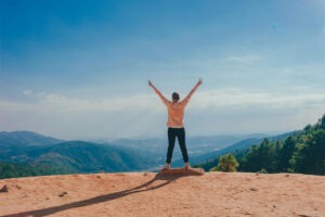 Person standing on top of mountain with hands in the air celebrating