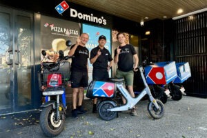 Three men standing at the front of a pizza shop with electric bikes