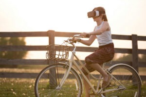 Female riding a bike outdoors with virtual reality goggles on.