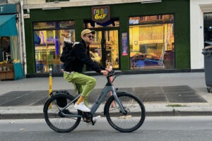 Man riding an ebike on street with dog in backpack.