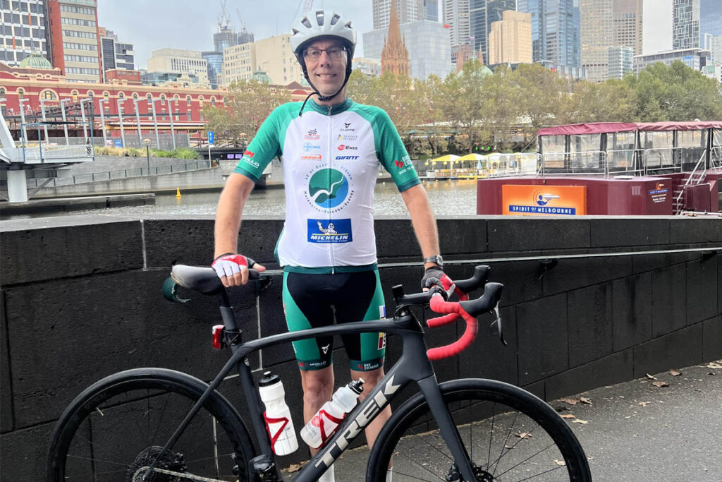 Man posing with bicycle in cycling attire.