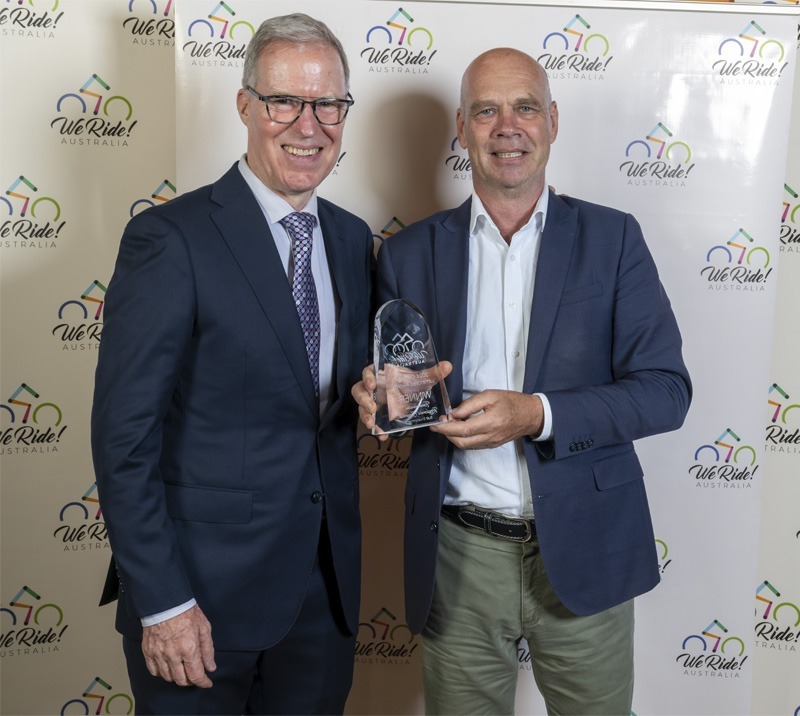 Two men wearing professional attire, one holding an award.