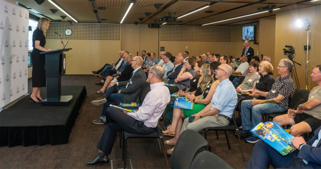 Group of people sitting in front of person speaking on stage.